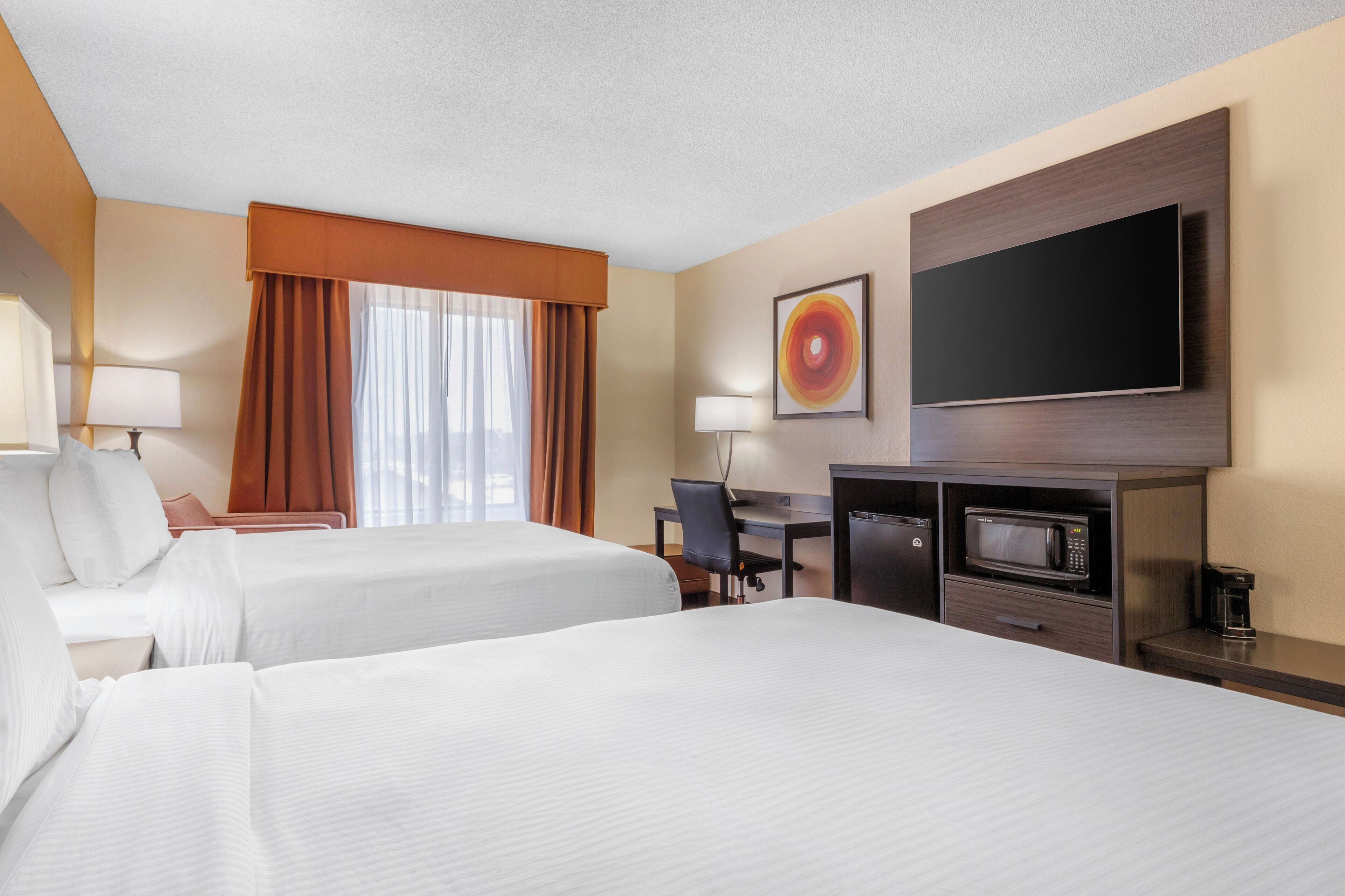 A hotel room with two beds, a desk, a TV, a microwave, and a coffee maker.