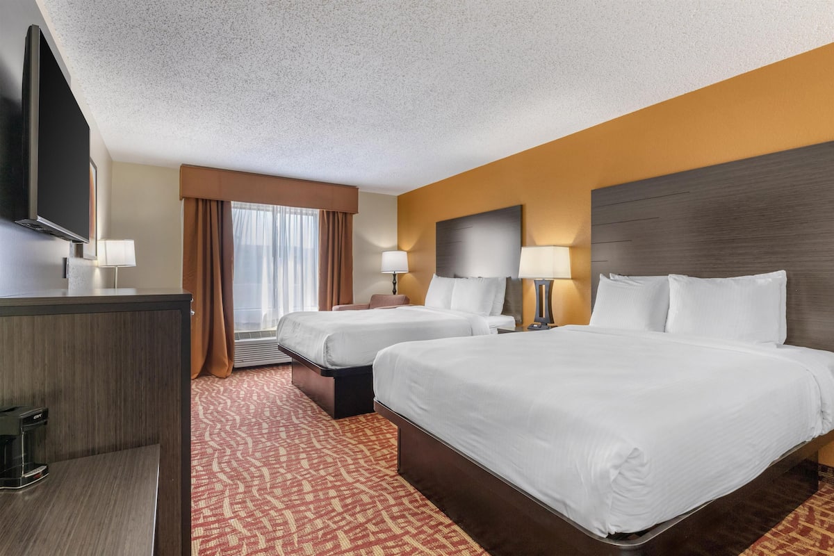 A hotel room with two beds, a TV, and a desk.