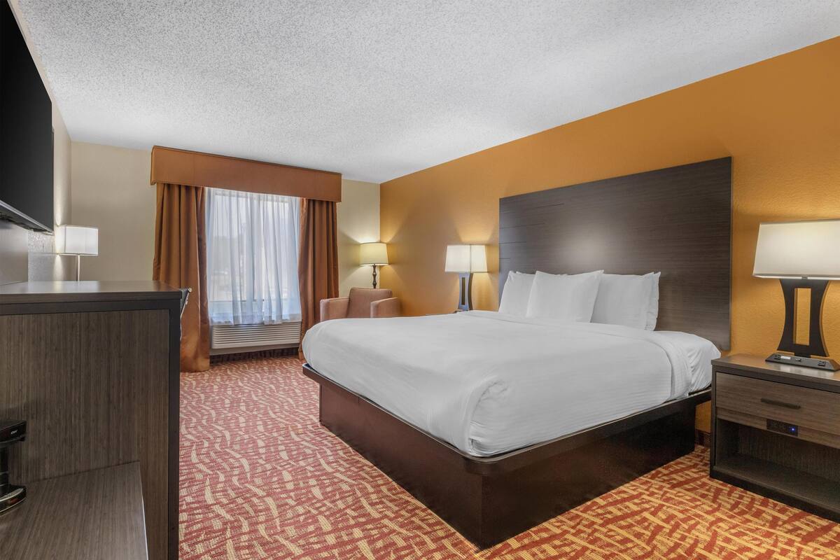 A hotel room with a large bed, bedside tables, a desk, and a flat-screen TV.