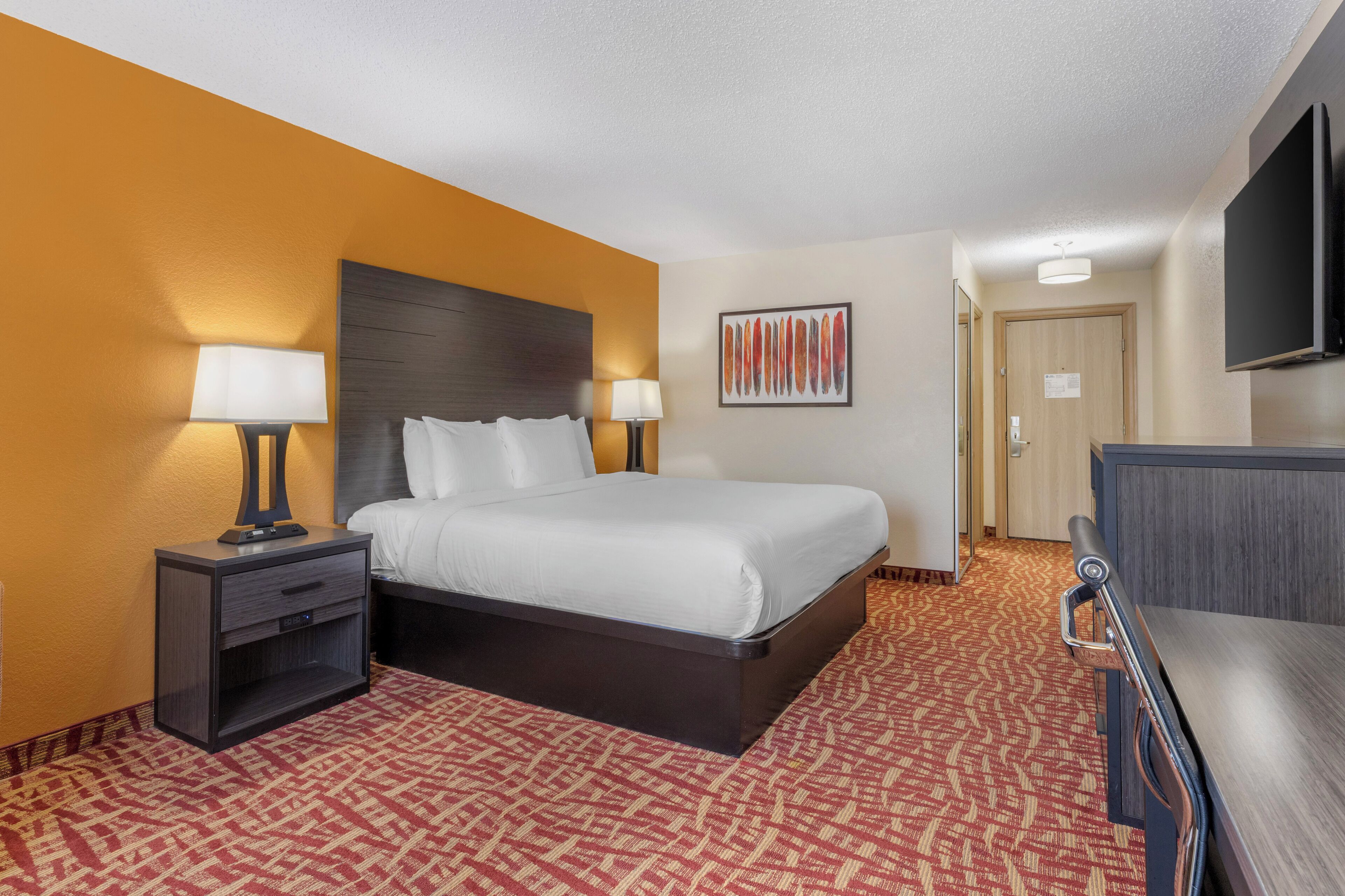 A hotel room with a bed, nightstands, a TV, and a patterned carpet.