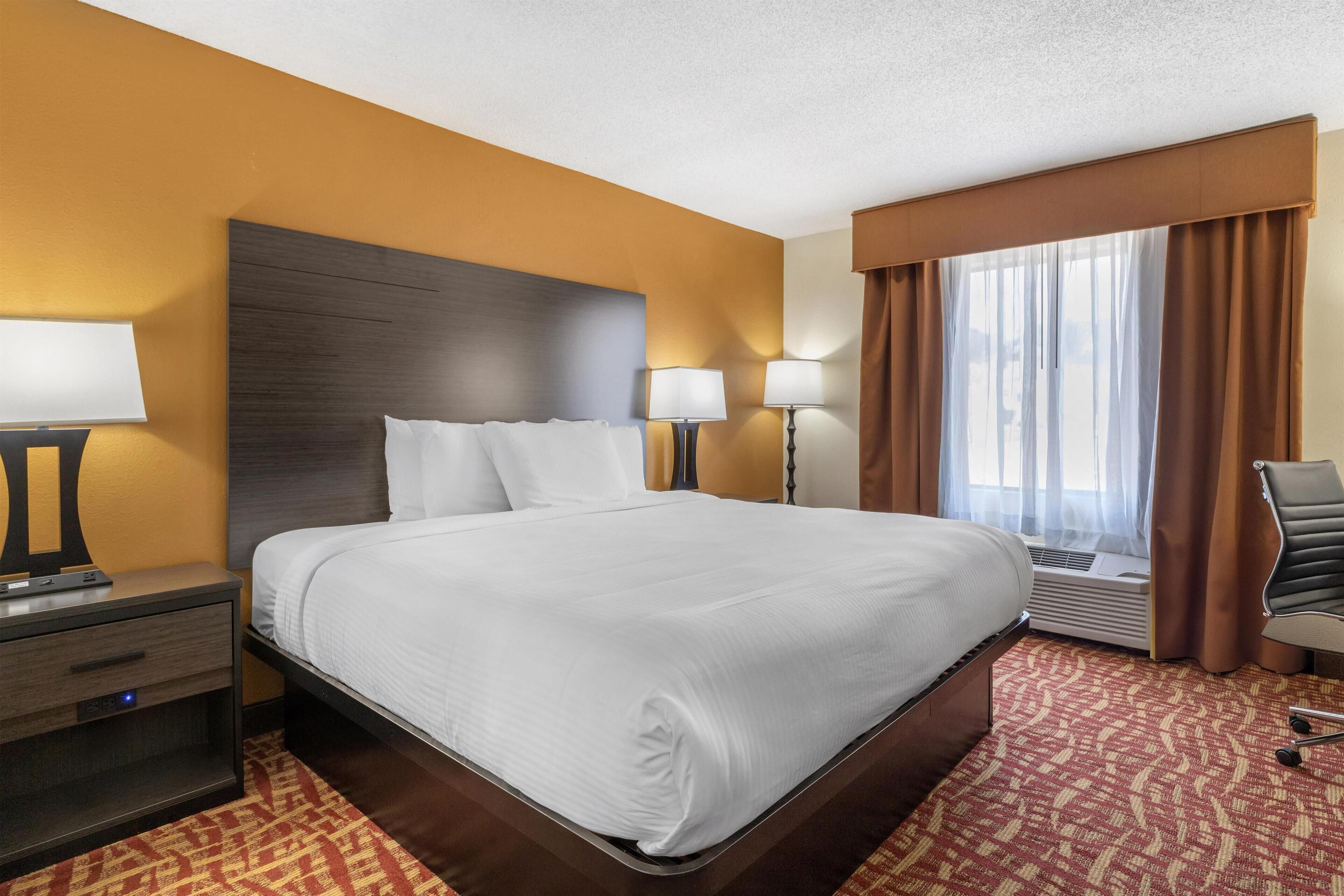 A hotel room with a large bed, two bedside tables with lamps, a chair, and a window with curtains.