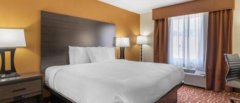 A hotel room with a large bed, two bedside tables with lamps, a chair, and a window with curtains.