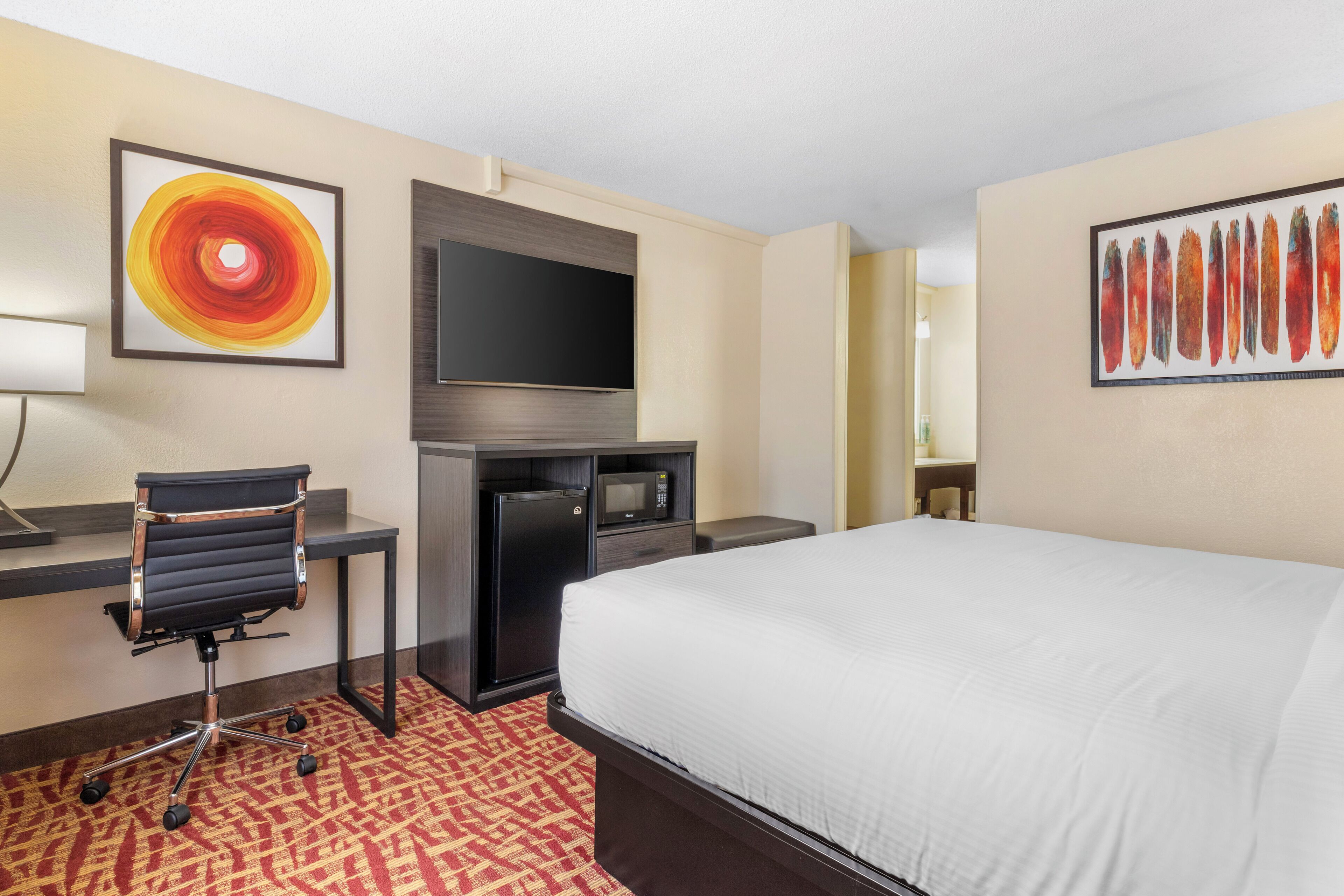 A hotel room with a bed, a desk with a chair, a television, and artwork on the walls.