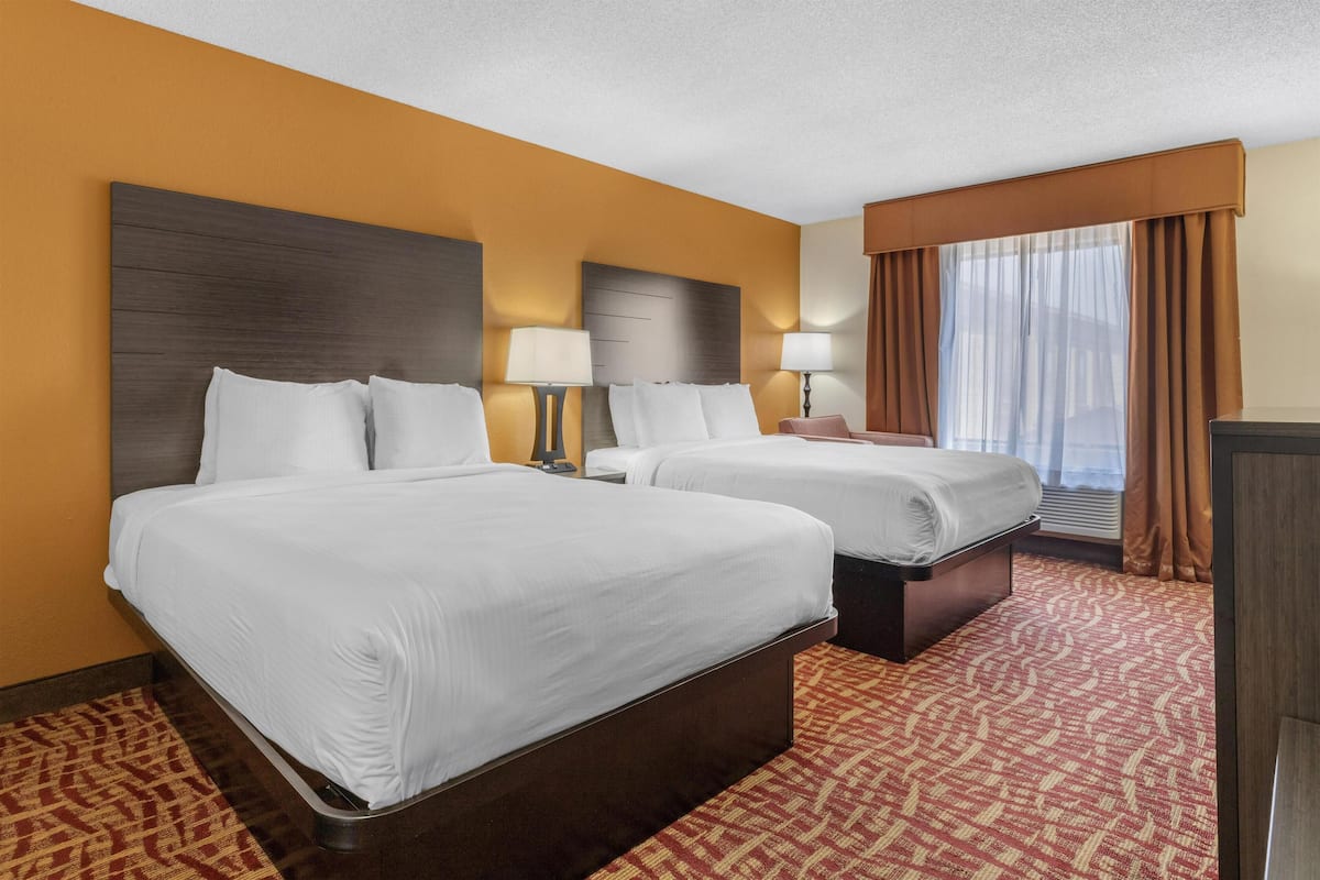 A hotel room with two beds, a wooden headboard, a red patterned carpet, and a window with curtains.