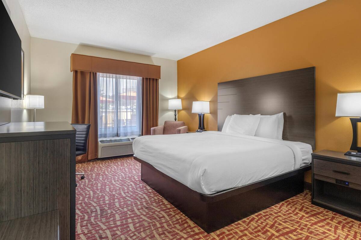 A hotel room with a large bed, two bedside tables with lamps, a desk, and a TV.