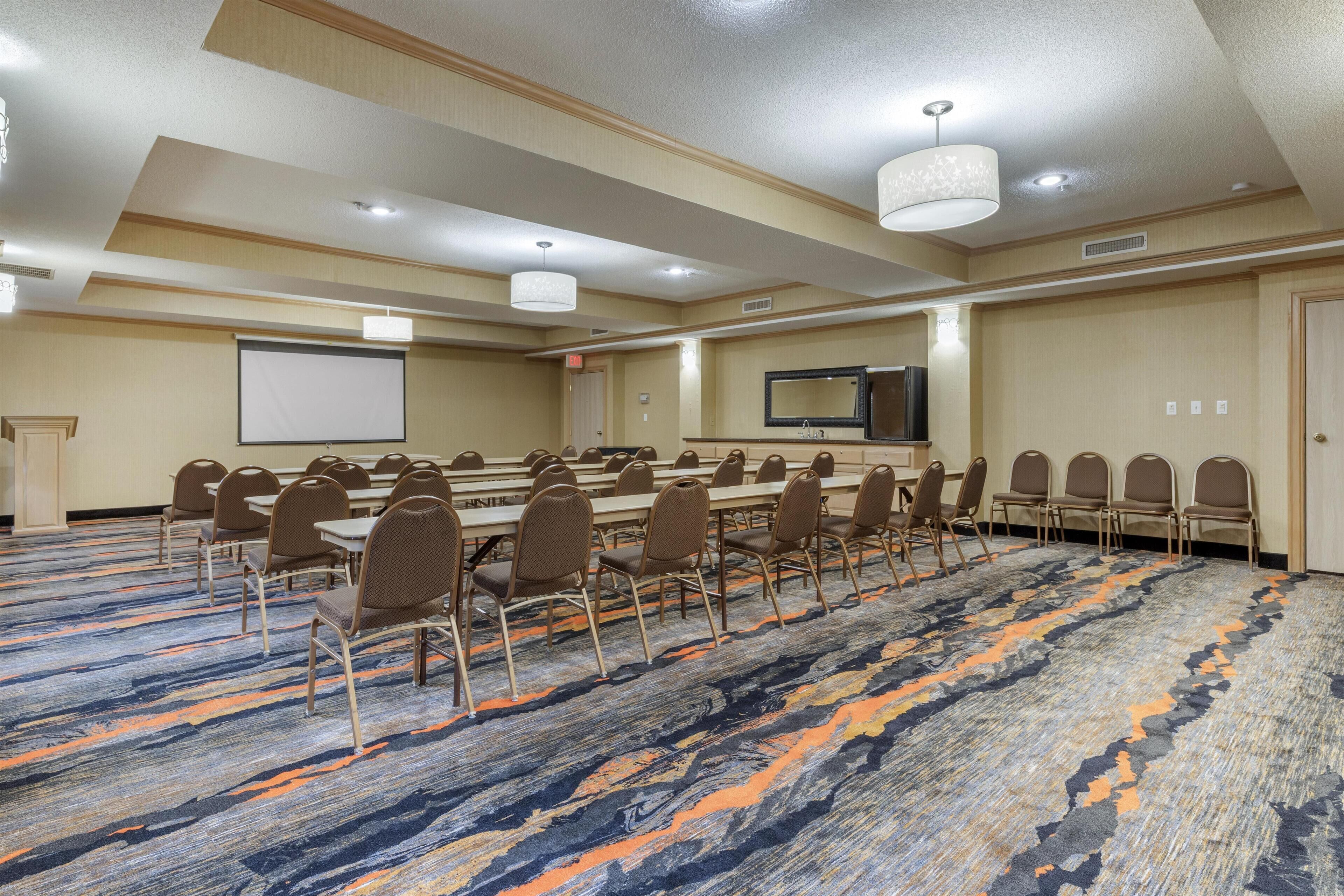 Un salón de conferencias con una gran mesa, sillas, una pantalla de proyector y una televisión.