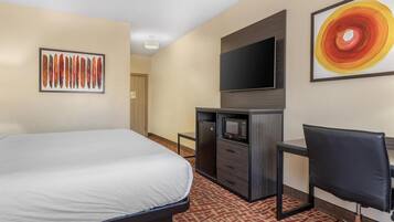 A hotel room with a bed, a desk with a chair, a television, and artwork on the walls.