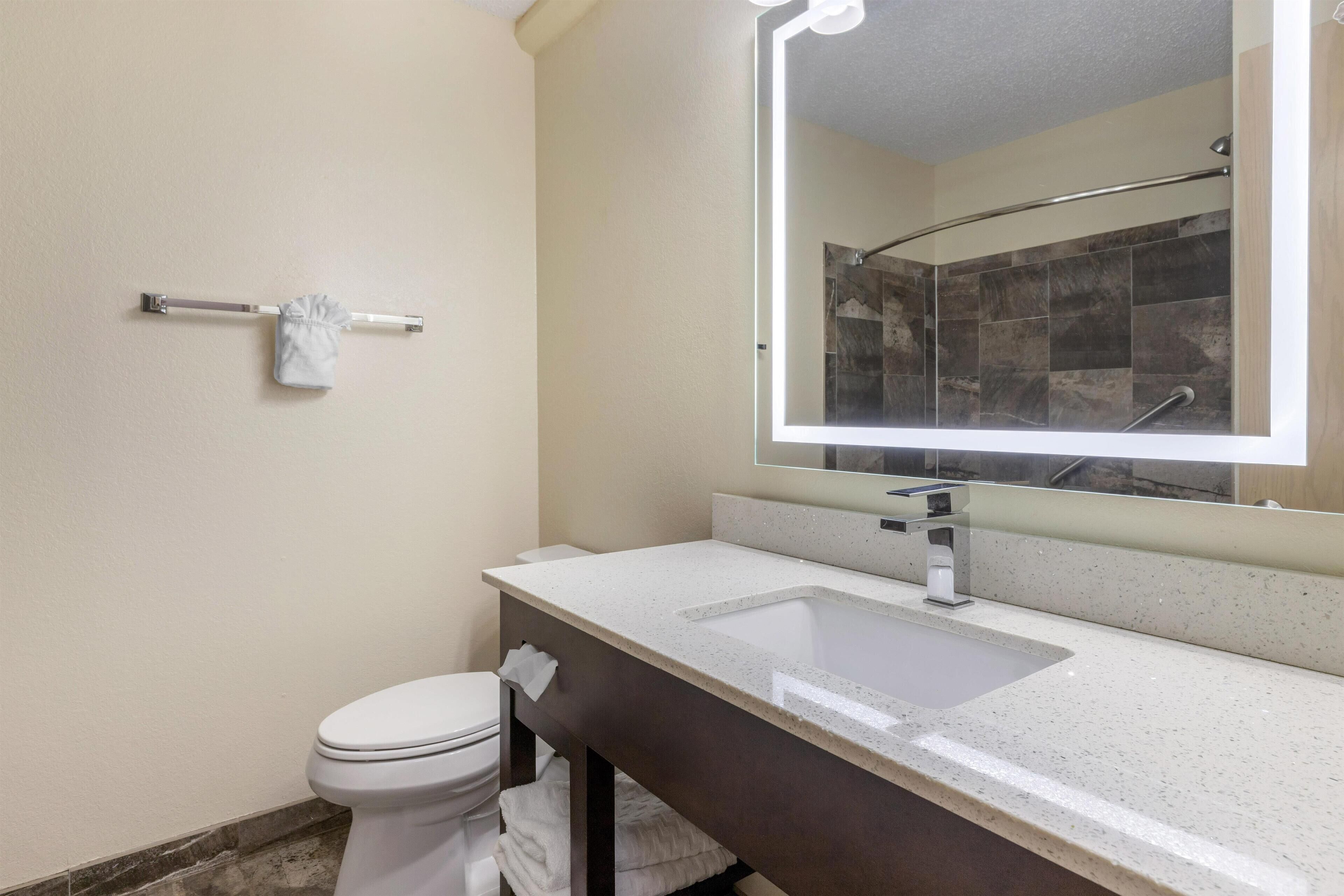 Un baño con un lavamanos blanco, un espejo con iluminación, un toallero y un inodoro.
