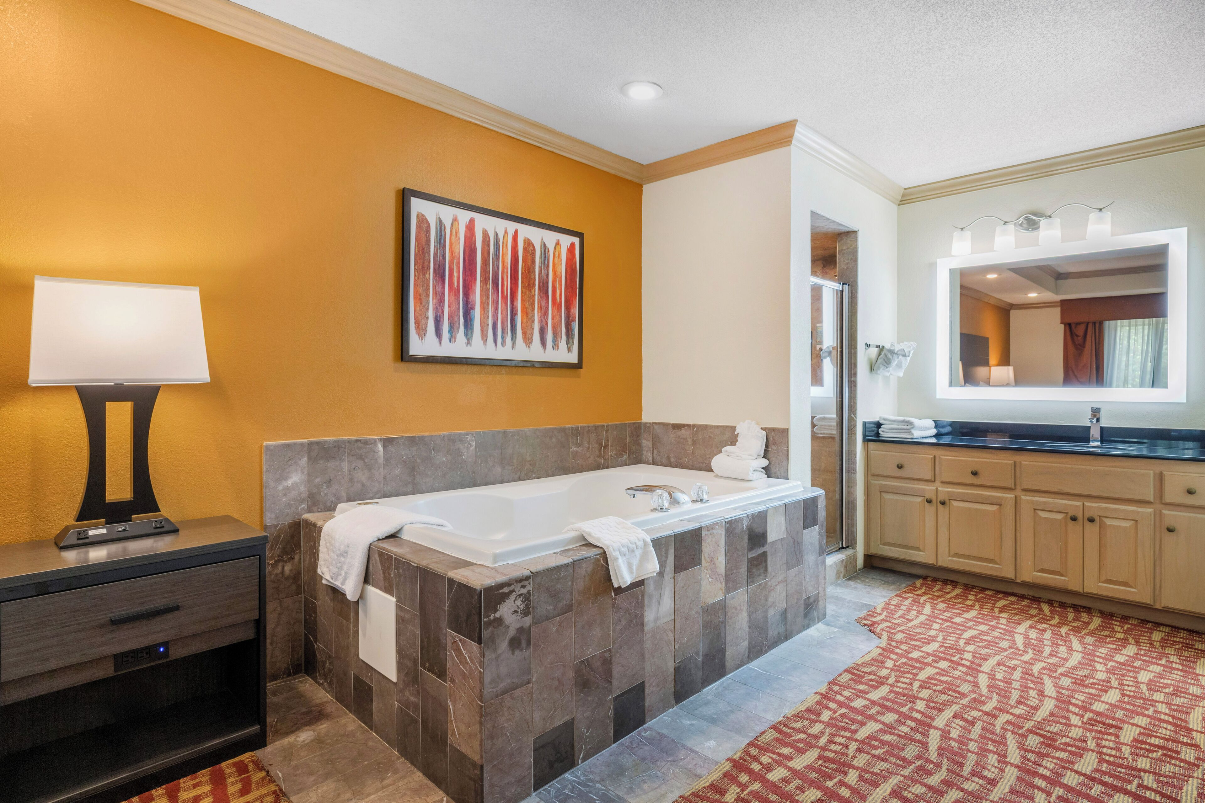 A modern bathroom with a bathtub, a vanity with a mirror, and a wall-mounted artwork.