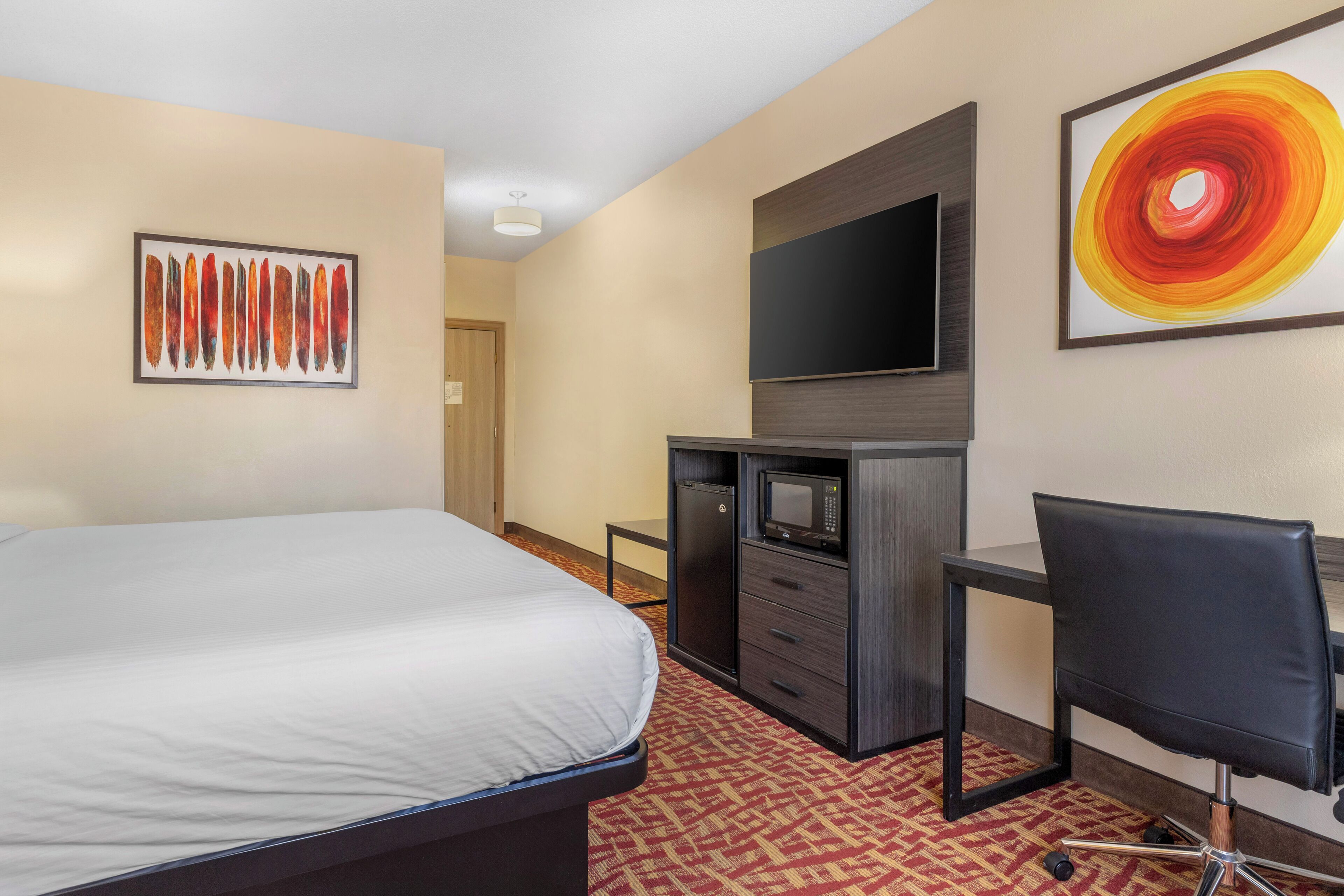 Una habitación de hotel con cama, escritorio con silla, televisor y obras de arte en las paredes.