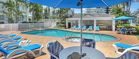 A poolside area with lounge chairs, a table, and umbrellas.