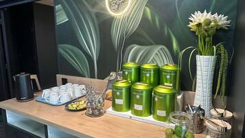 Una barra con un cartel de café, un jarrón de flores y varias latas verdes con la etiqueta 'Palais des Thés'.