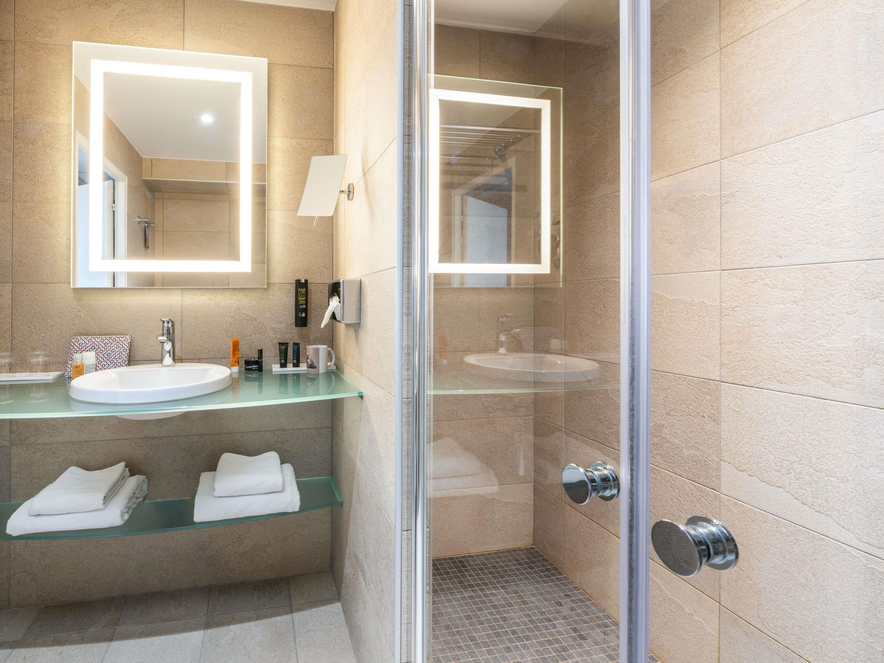 Un baño moderno con cabina de ducha de vidrio, encimera de vidrio y un espejo grande.