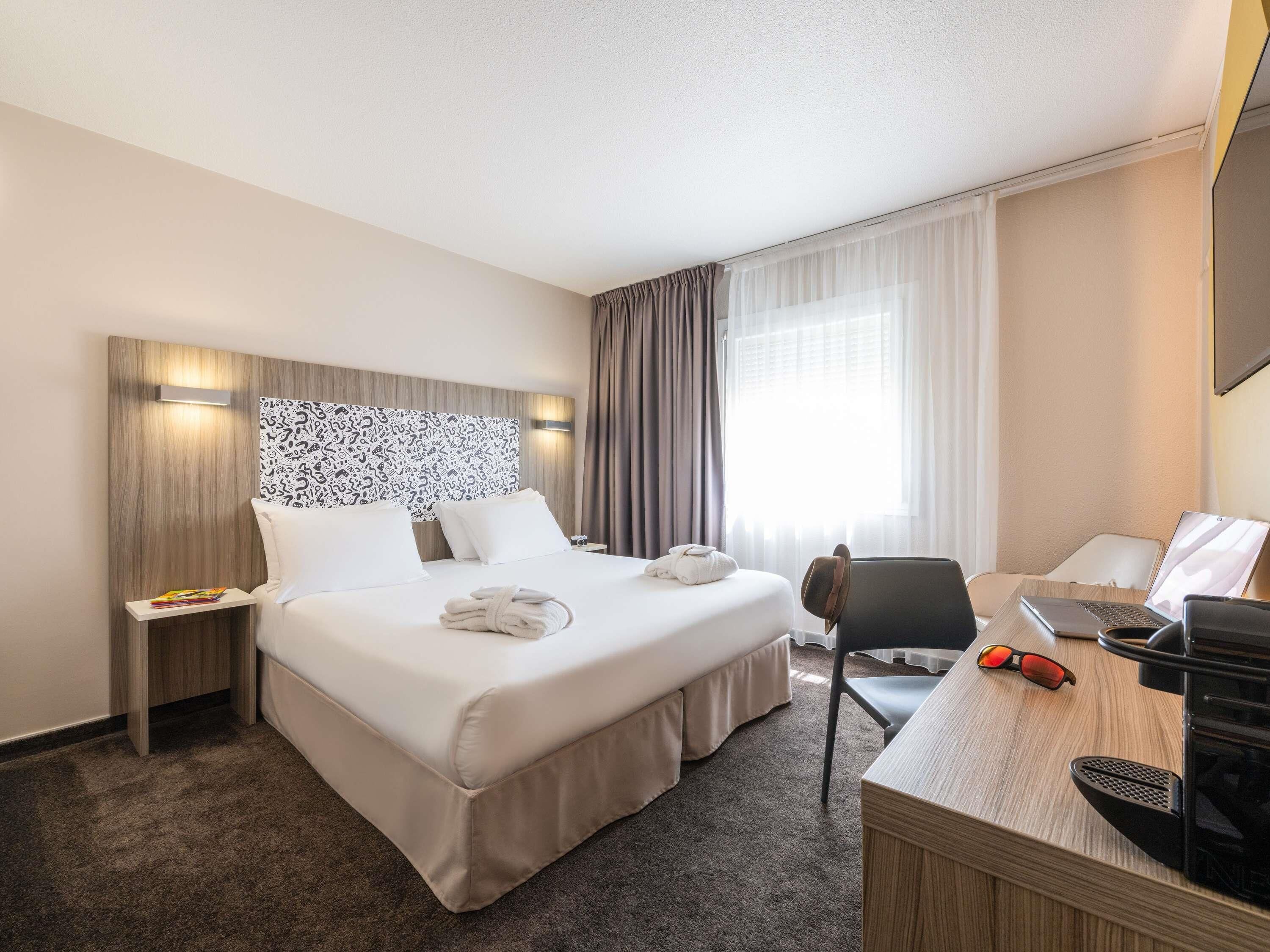 Quarto de hotel com uma cama grande, uma mesa com um laptop e uma cadeira.