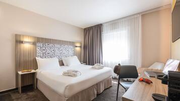 Quarto de hotel com uma cama grande, uma mesa com um laptop e uma cadeira.