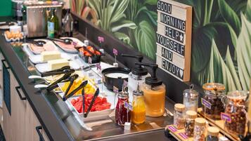 A buffet with various food items and condiments, a sign with a motivational message, and a green leafy wall in the background.
