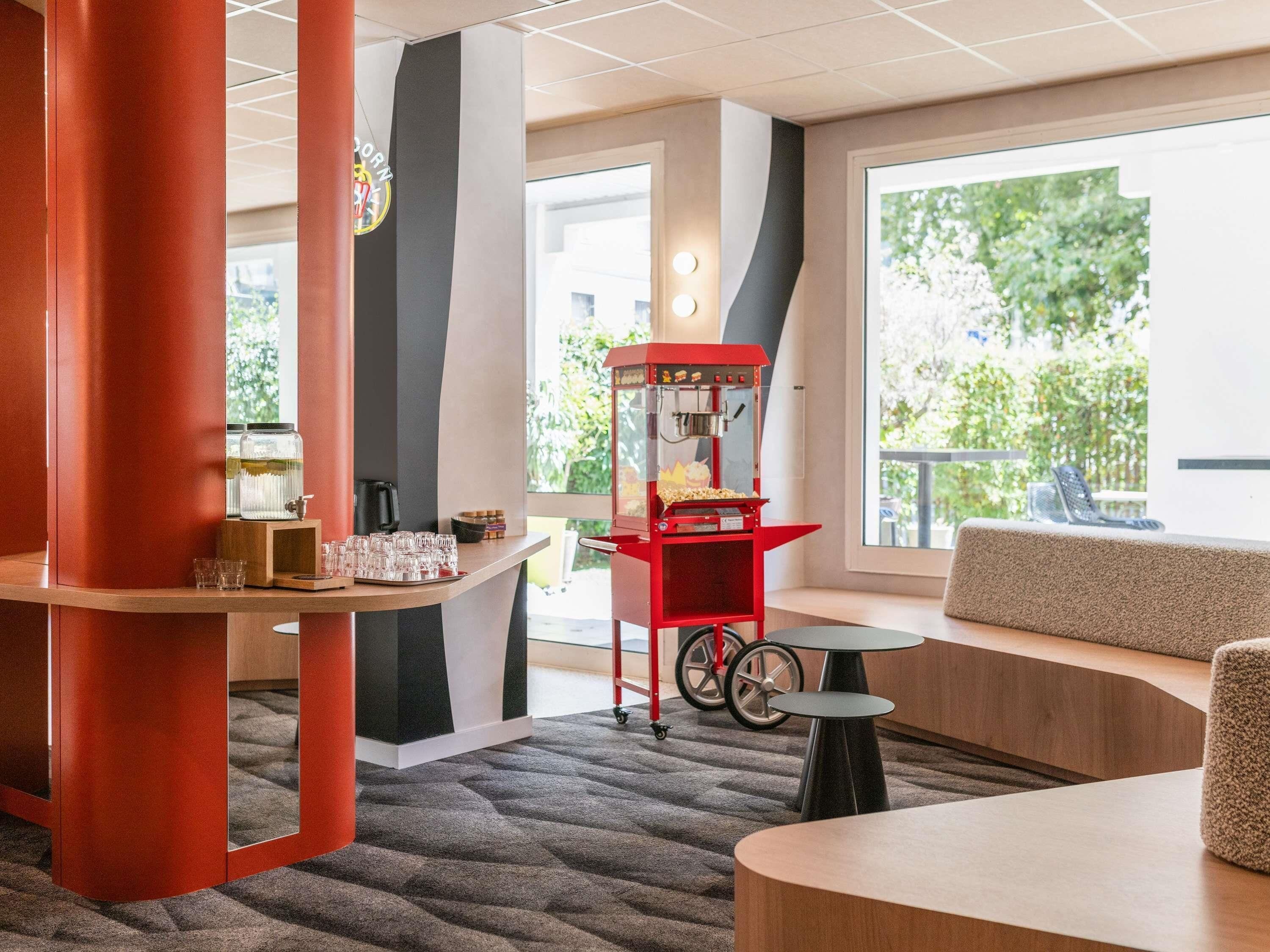 A modern interior with a seating area, a popcorn machine, and a window with a view of greenery.