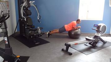 A gym with exercise equipment, a wall with a window, and a person performing a workout.