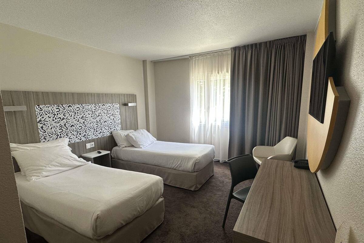 Habitación de hotel con dos camas, un escritorio, una silla, un televisor y una ventana con cortinas.