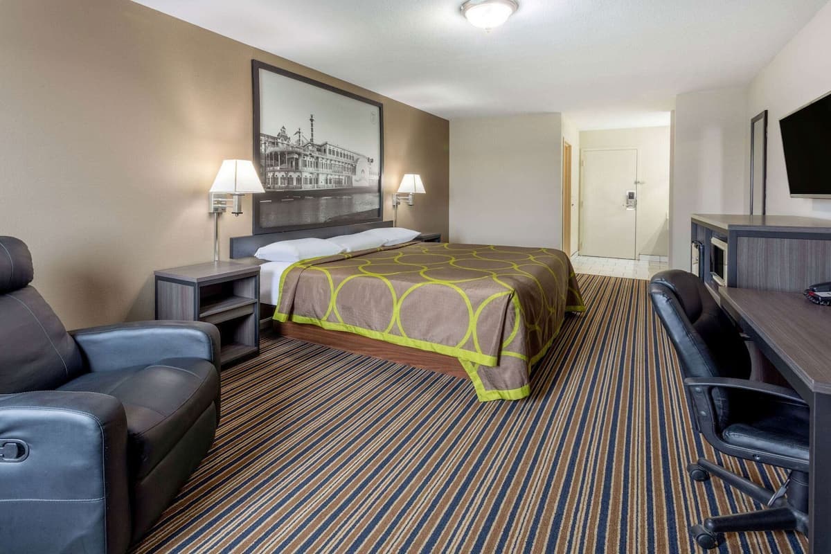 A hotel room with a bed, a desk, a chair, a TV, and a framed picture on the wall.
