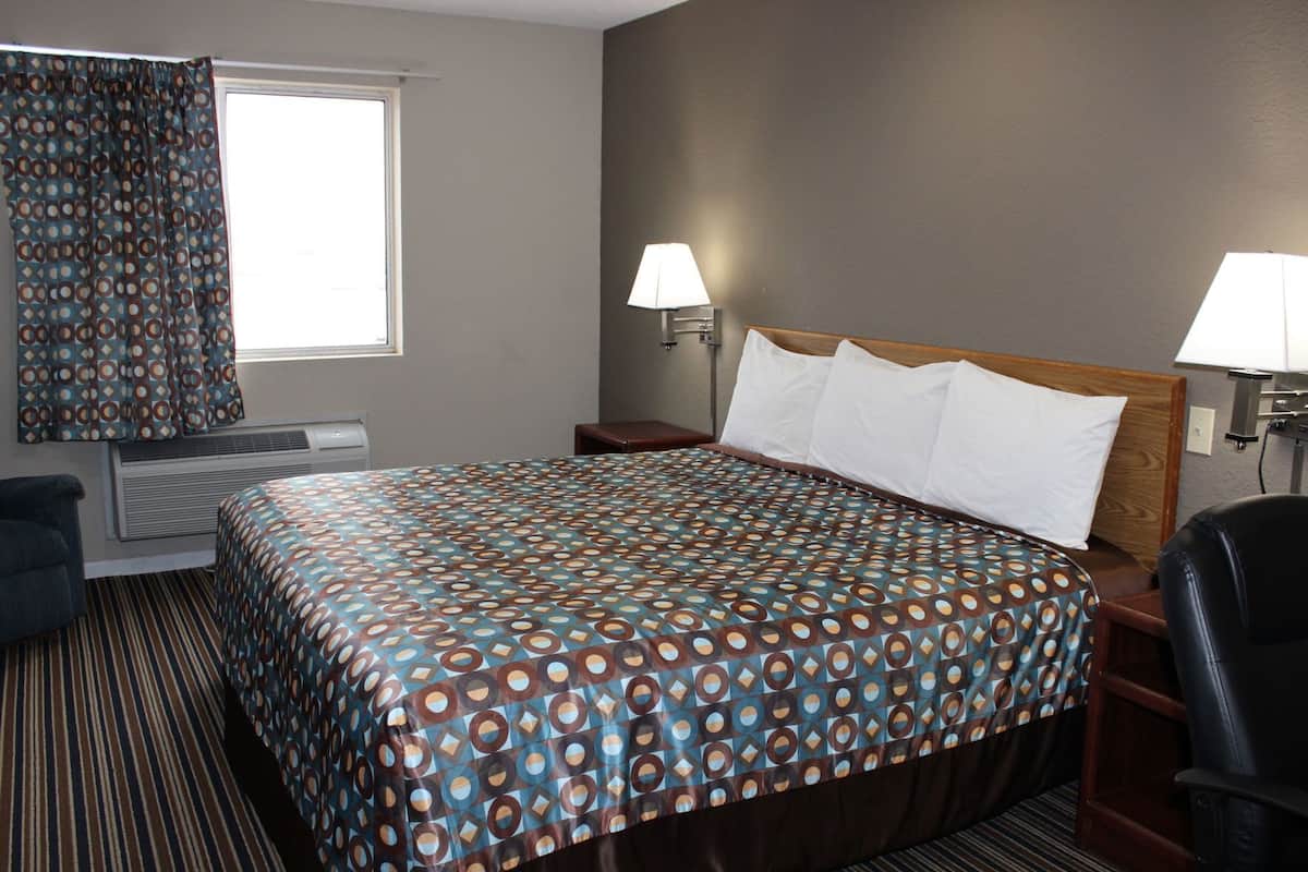 A hotel room with a bed, two bedside lamps, a chair, a window with curtains, and a radiator.