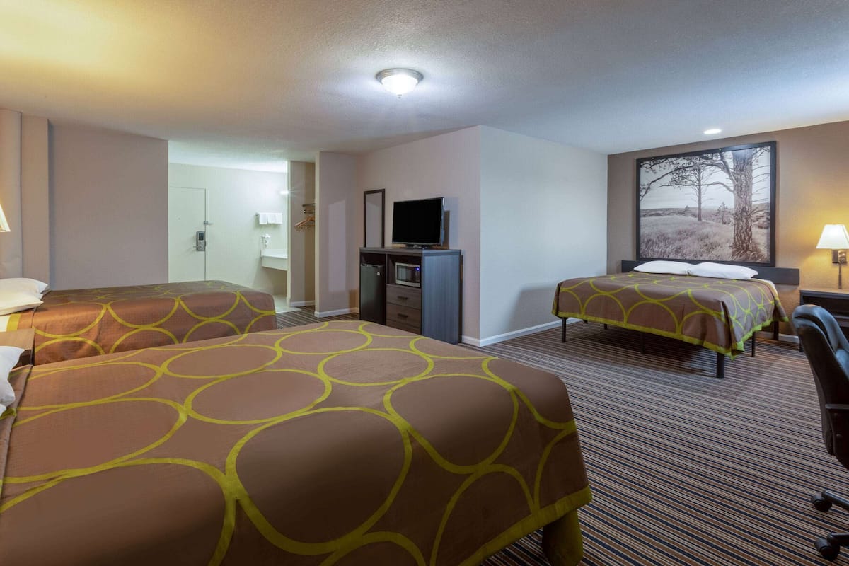 A hotel room with two beds, a desk, a television, and a bathroom visible through an open door.