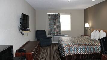 A hotel room with a bed, a desk with a telephone, a chair, a television mounted on the wall, and a window with curtains.