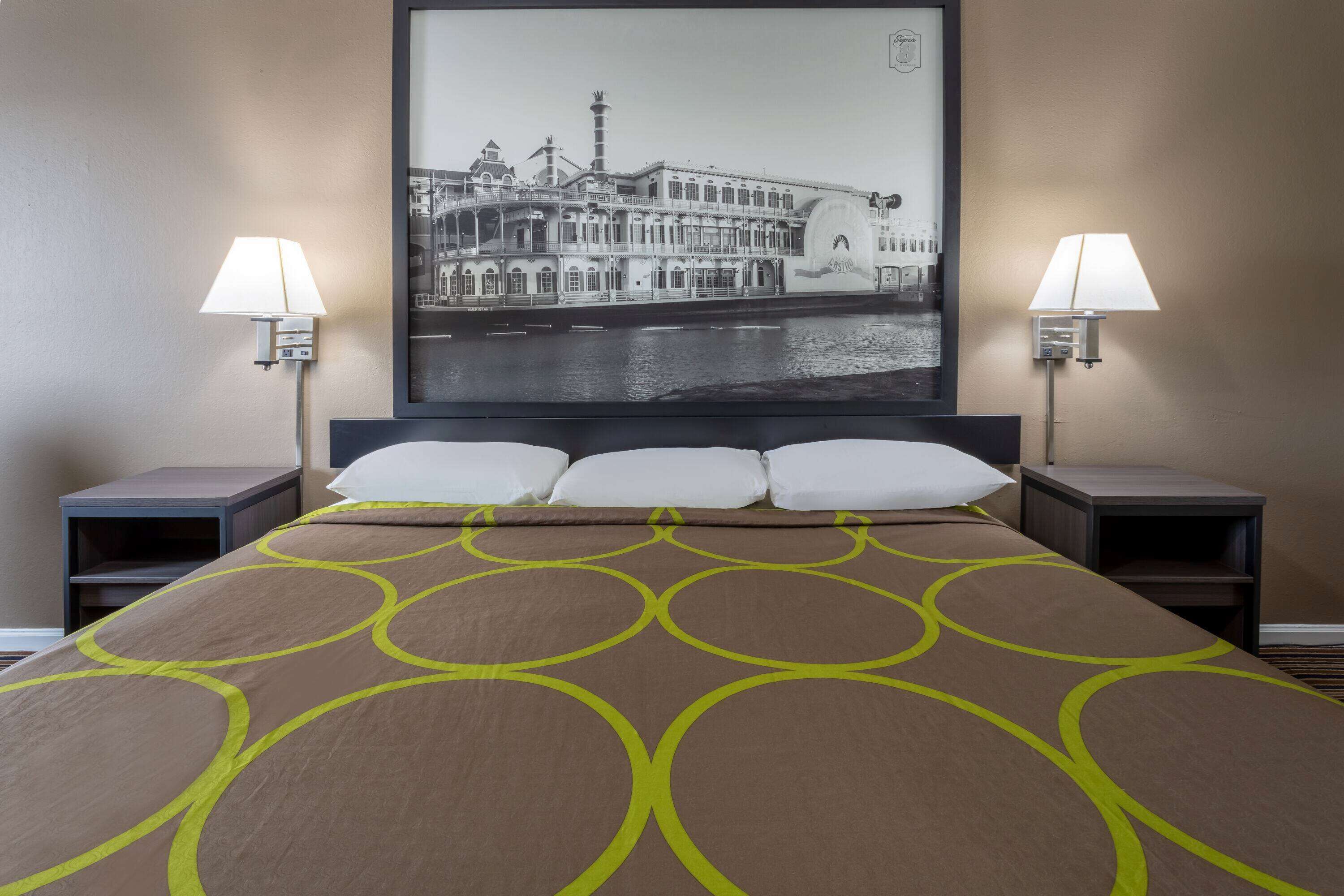 A hotel room with a large bed, two bedside tables, two lamps, and a framed picture of a building on the wall.