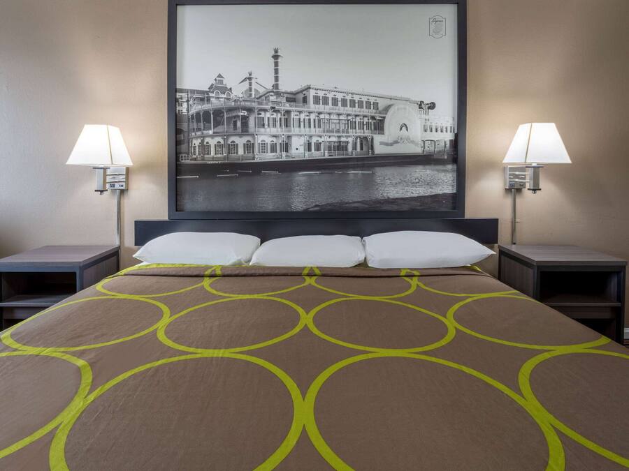 A hotel room with a large bed, two bedside tables, two lamps, and a framed picture of a building on the wall.