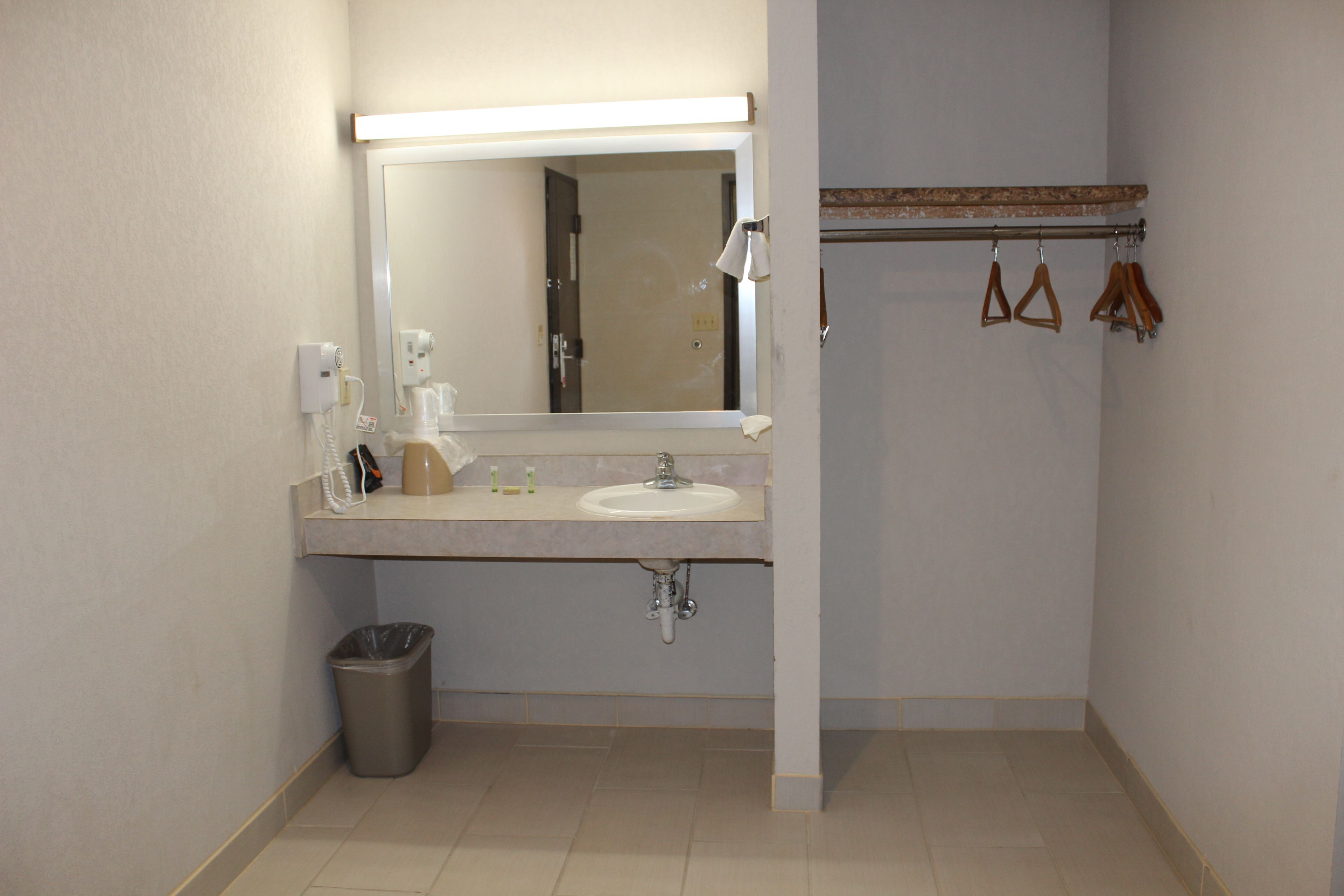 A bathroom with a sink, mirror, and hanging clothes rack.