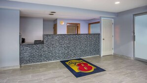 Un hall d’hôtel avec un comptoir d’accueil, un tapis orné du logo Super 8 et une porte donnant sur une autre pièce.