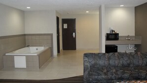Une chambre d’hôtel dotée d’une grande baignoire, d’un canapé, d’une kitchenette équipée d’un four à micro-ondes et d’une porte donnant sur une autre pièce.