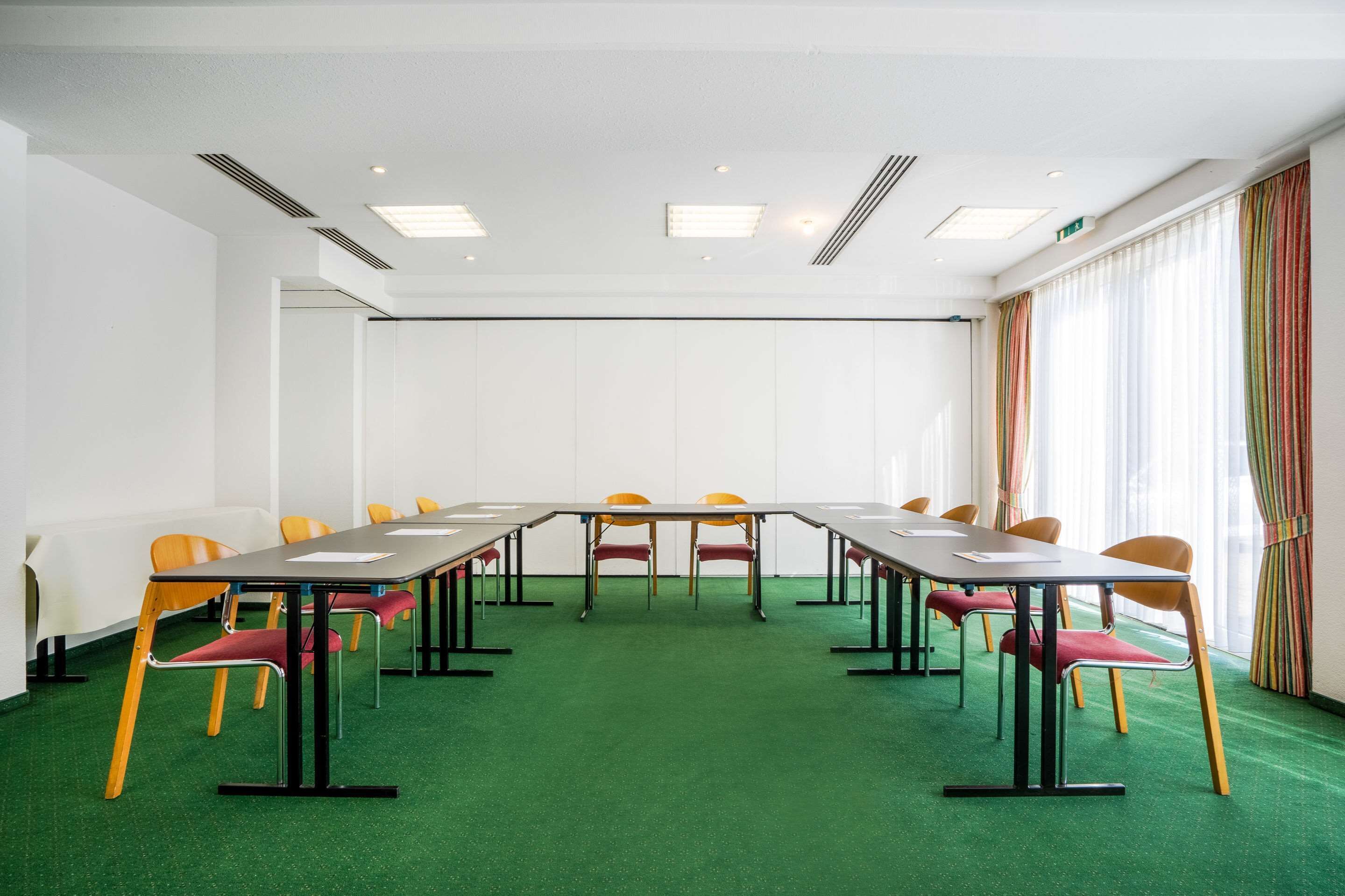 Ein Konferenzraum mit langem Tisch, mehreren Stühlen und einem grünen Teppich.