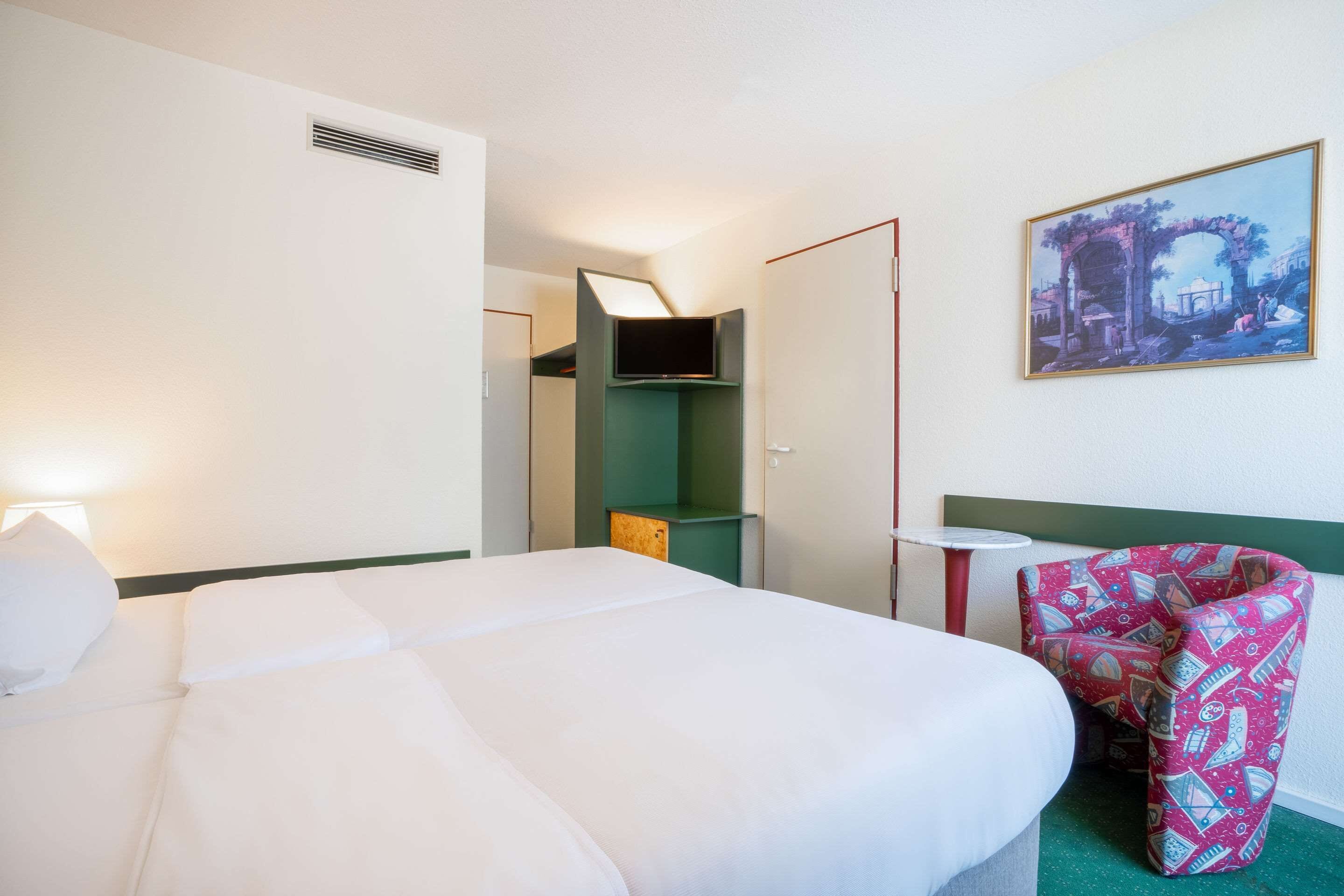 A hotel room with a large bed, a desk, a chair, and a painting on the wall.