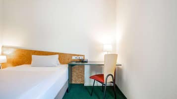 A hotel room with a bed, a desk, a chair, and a lamp.