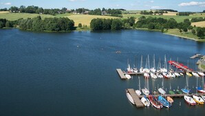 Un puerto deportivo con barcos amarrados, rodeado de campos verdes y árboles.