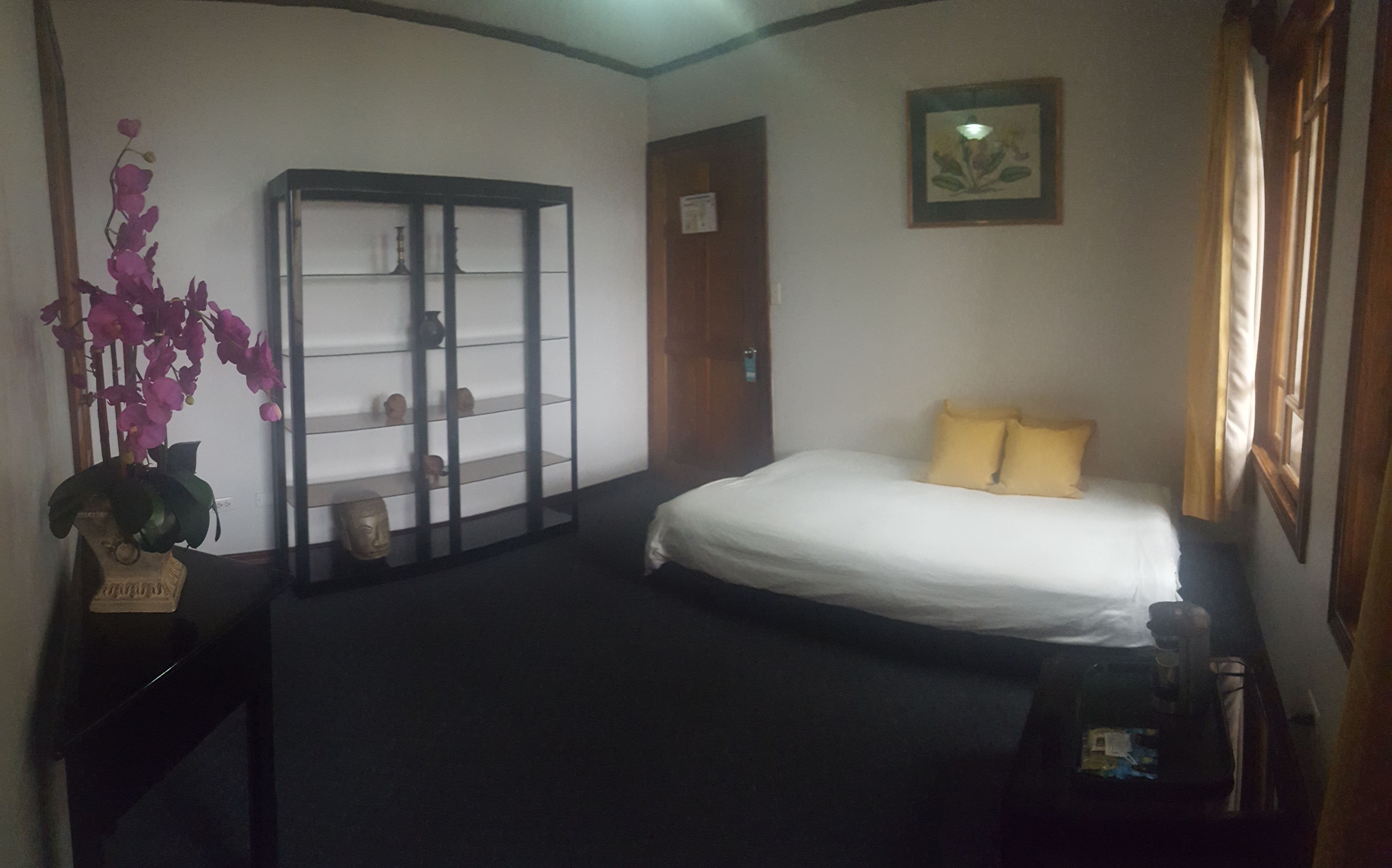 Ein Hotelzimmer mit Bett, Nachttisch, einer Ablage mit Dekoration, einer Tür und einem Fenster mit Vorhängen.