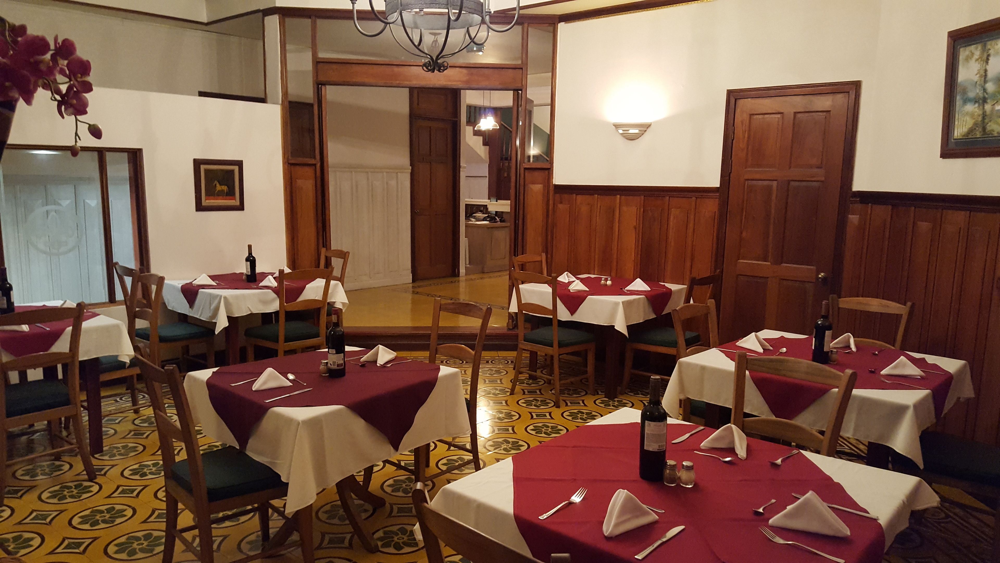 A dining area with multiple tables set for service, wooden chairs, and a patterned floor.