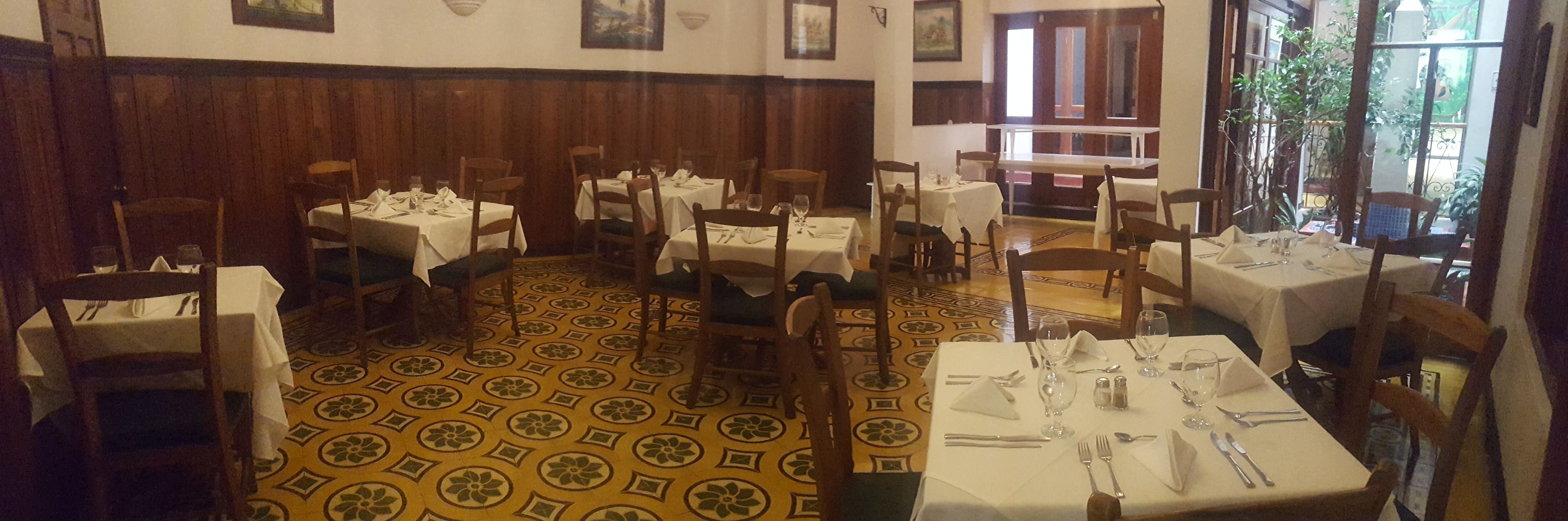 A restaurant with multiple tables set for dining, featuring a patterned floor and wooden paneling on the walls.