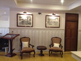 Una habitación con dos sillones tapizados, una mesita y un atril de madera. Encima de los sillones hay dos cuadros enmarcados en la pared.