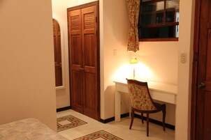 A room with a wooden wardrobe, a desk with a chair, and a lamp.