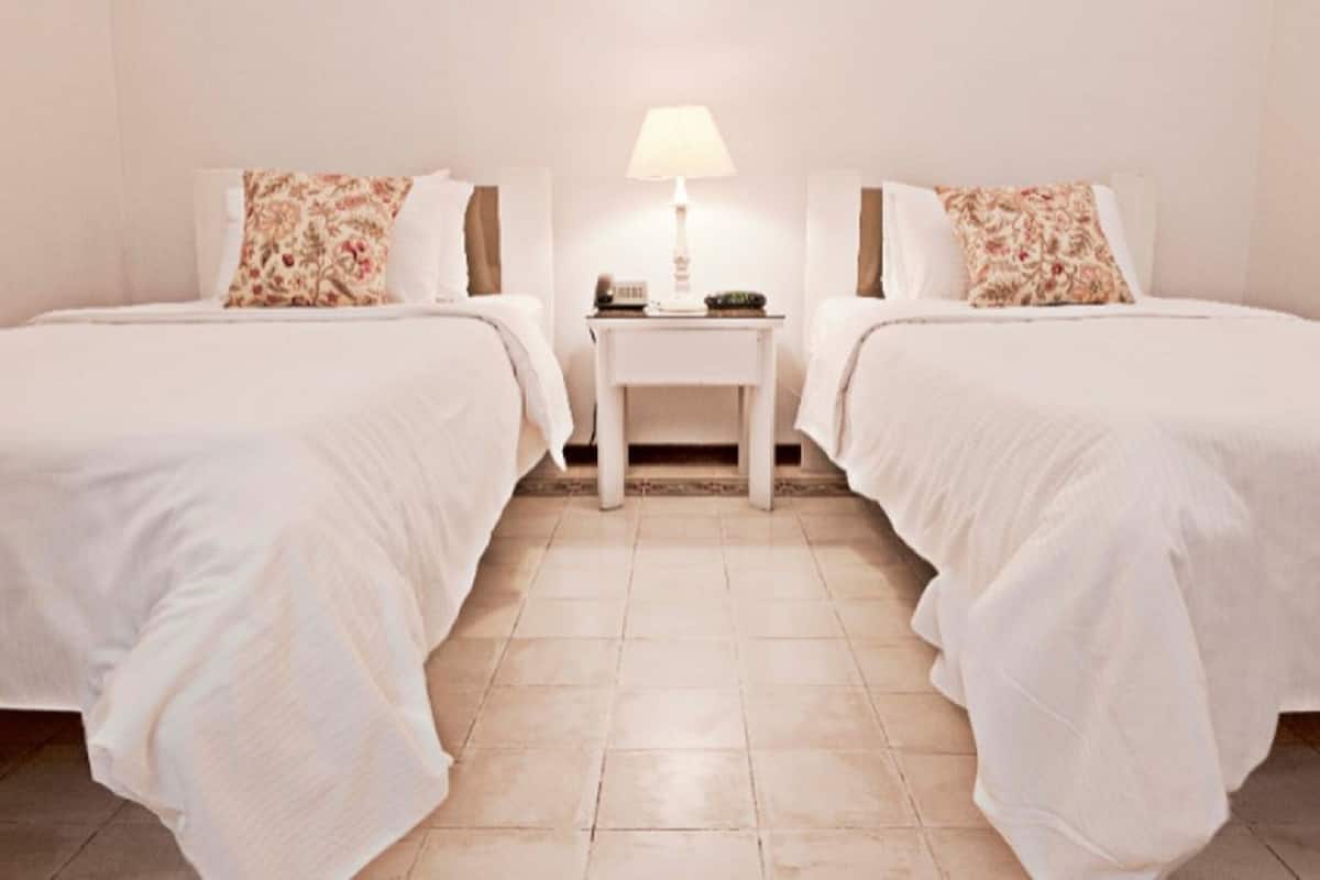 A hotel room with two single beds, a small bedside table with a lamp, and a tiled floor.