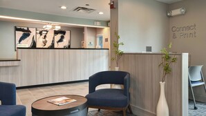 Un espace d’accueil avec un comptoir en bois, une chaise bleue, un vase blanc contenant une plante et un panneau indiquant « Connectez-vous et imprimez ».