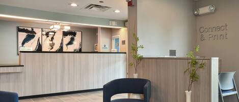 A reception area with a wooden reception desk, a blue chair, a white vase with a plant, and a sign that reads "Connect & Print".
