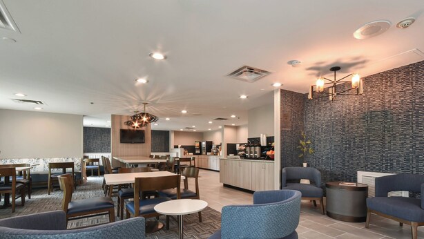 Un hall d’hôtel moderne comprenant un espace repas, une cuisine et un coin salon avec des fauteuils bleus.