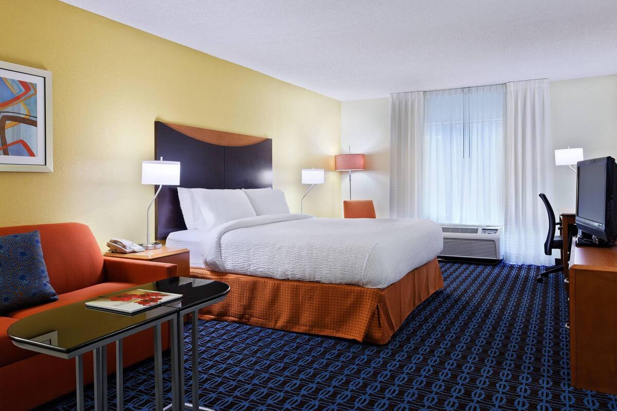 A hotel room with a bed, a desk, a chair, a TV, and a window with curtains.