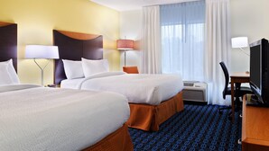 Une chambre d’hôtel avec deux lits, un bureau avec un ordinateur, une chaise, une lampe et une fenêtre avec des rideaux.