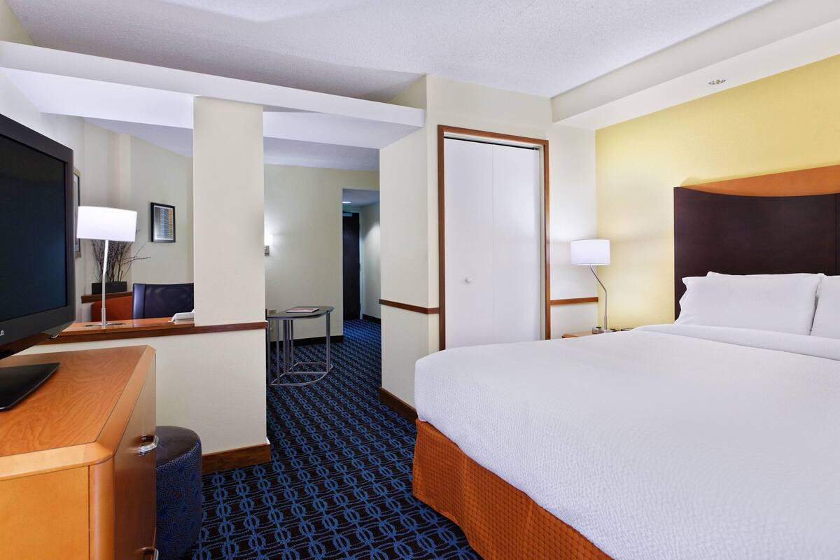A hotel room with a large bed, a desk with a computer, a television, and a small table.