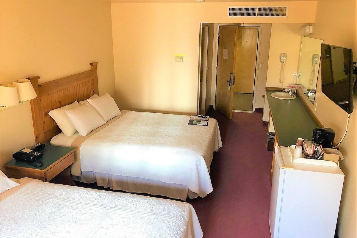 A hotel room with two beds, a desk with a telephone, a mirror, and a small kitchenette.