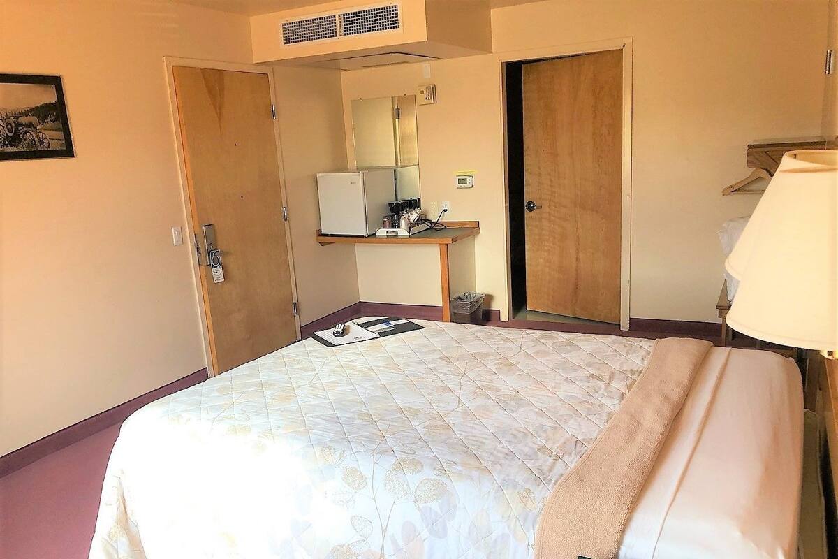 A hotel room with a bed, a desk with a computer, a mirror, and a wardrobe.